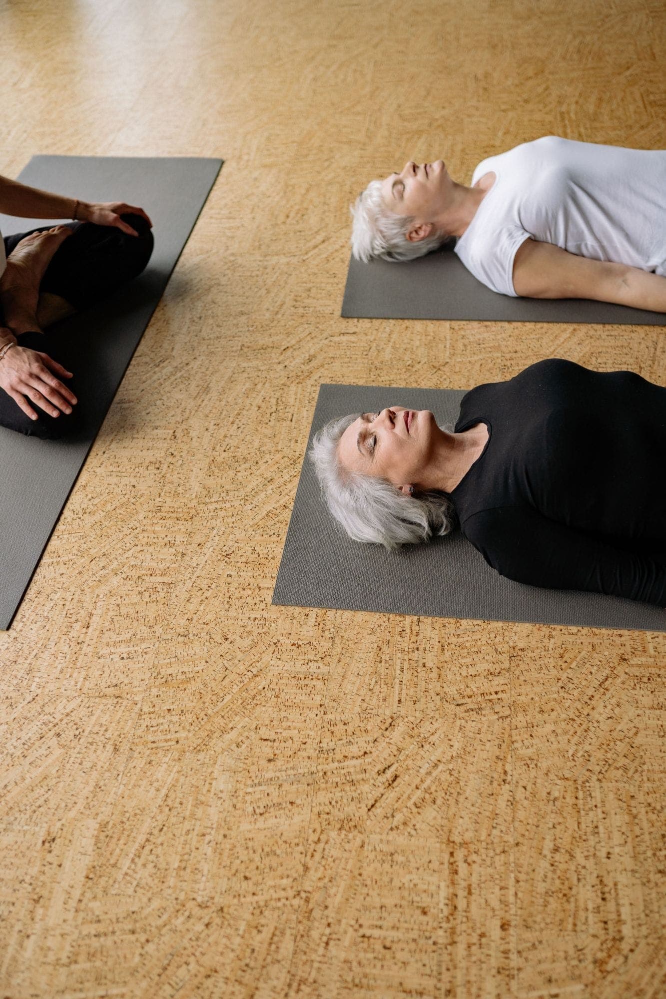 Two people lying at rest on mats while a teacher sits beside them