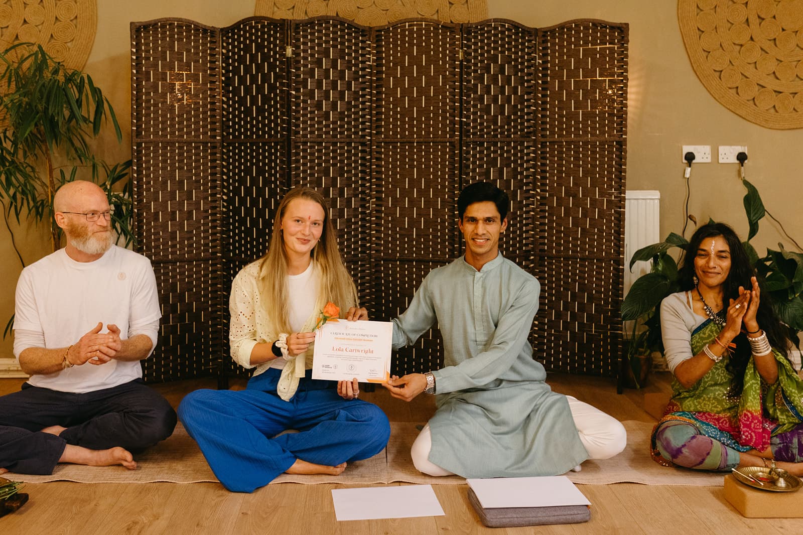 A graduate holds up her certificate beside Yogi Madhav as the teachers applaud