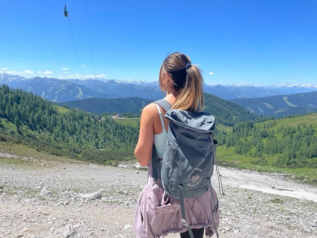A hiker with a backpack looking out over a green alpine valley