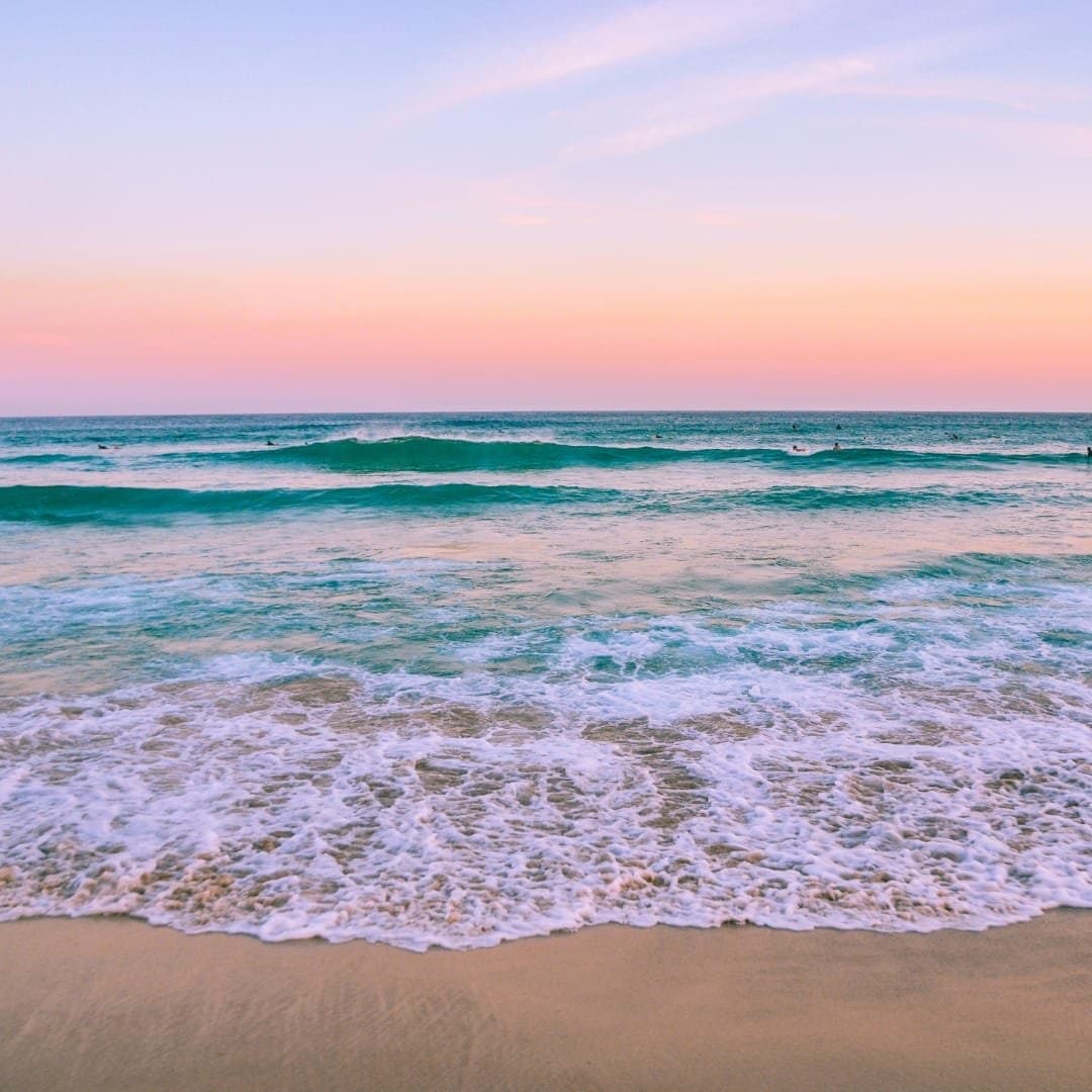Waves washing onto the sand under a pastel sky
