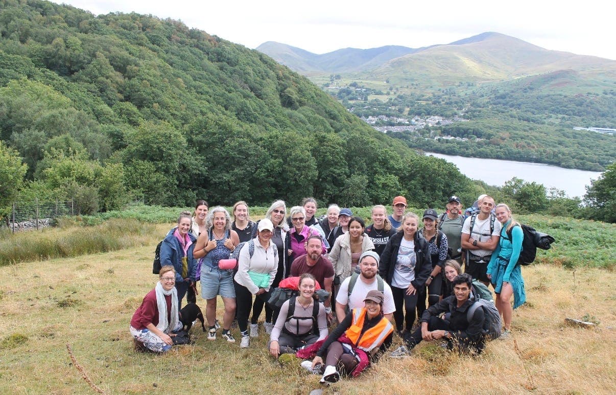 A group of walkers with yoga mats gathered on a hillside above Llyn Padarn, with mountains behind