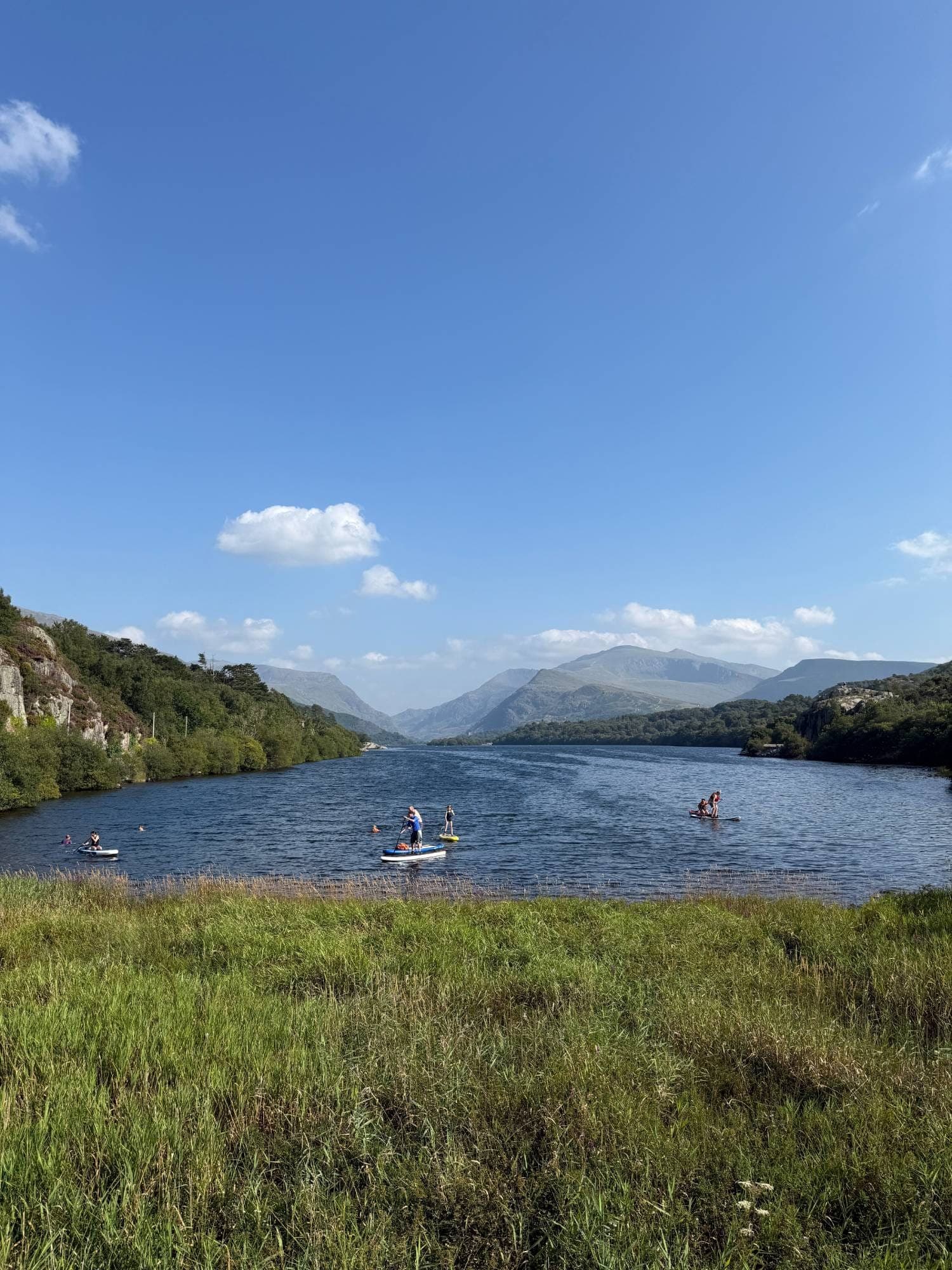 Paddleboarders on the calm lake in its mountain valley, under a clear blue sky
