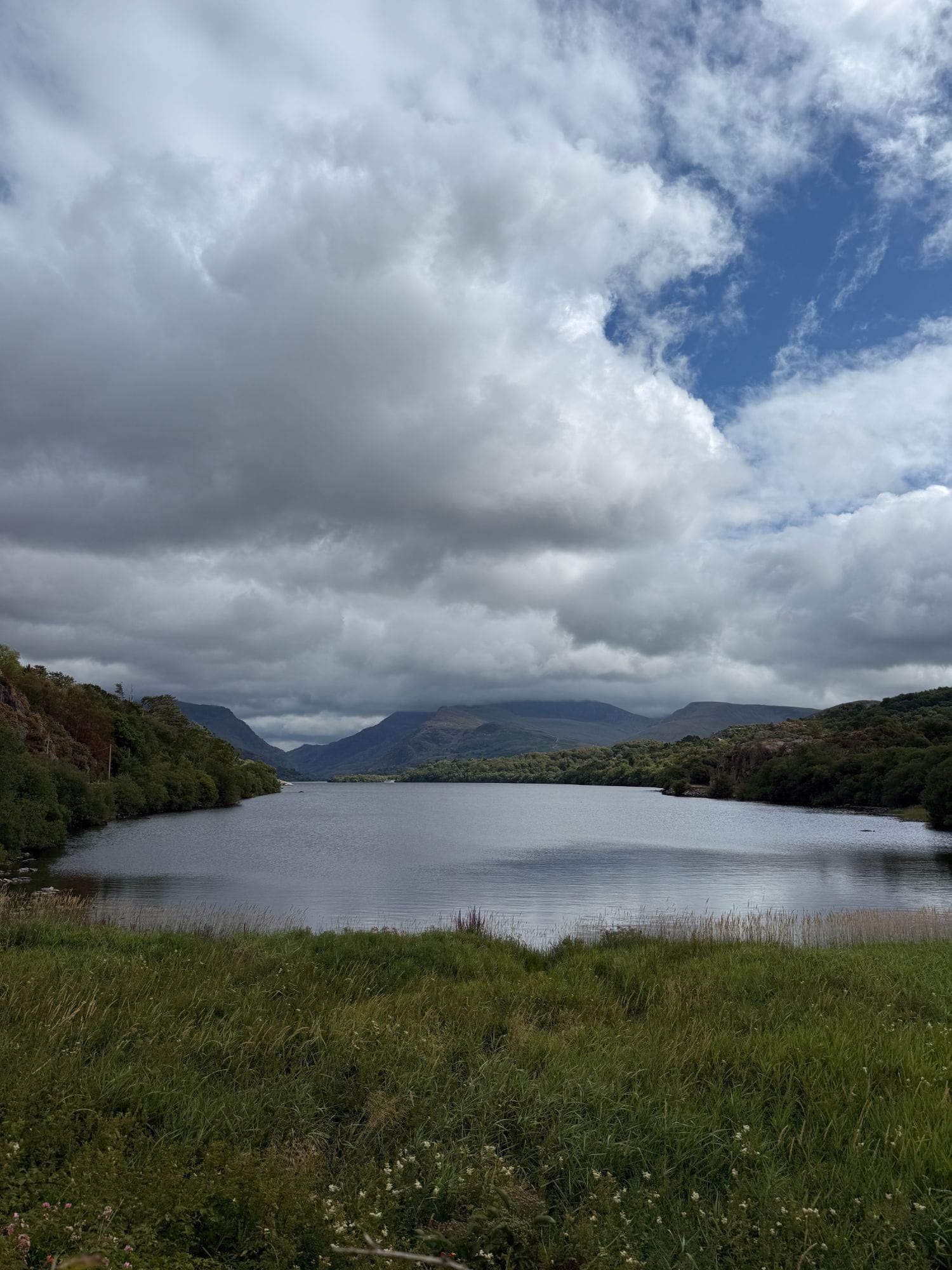 The long lake between wooded hills, with mountains beneath heavy cloud