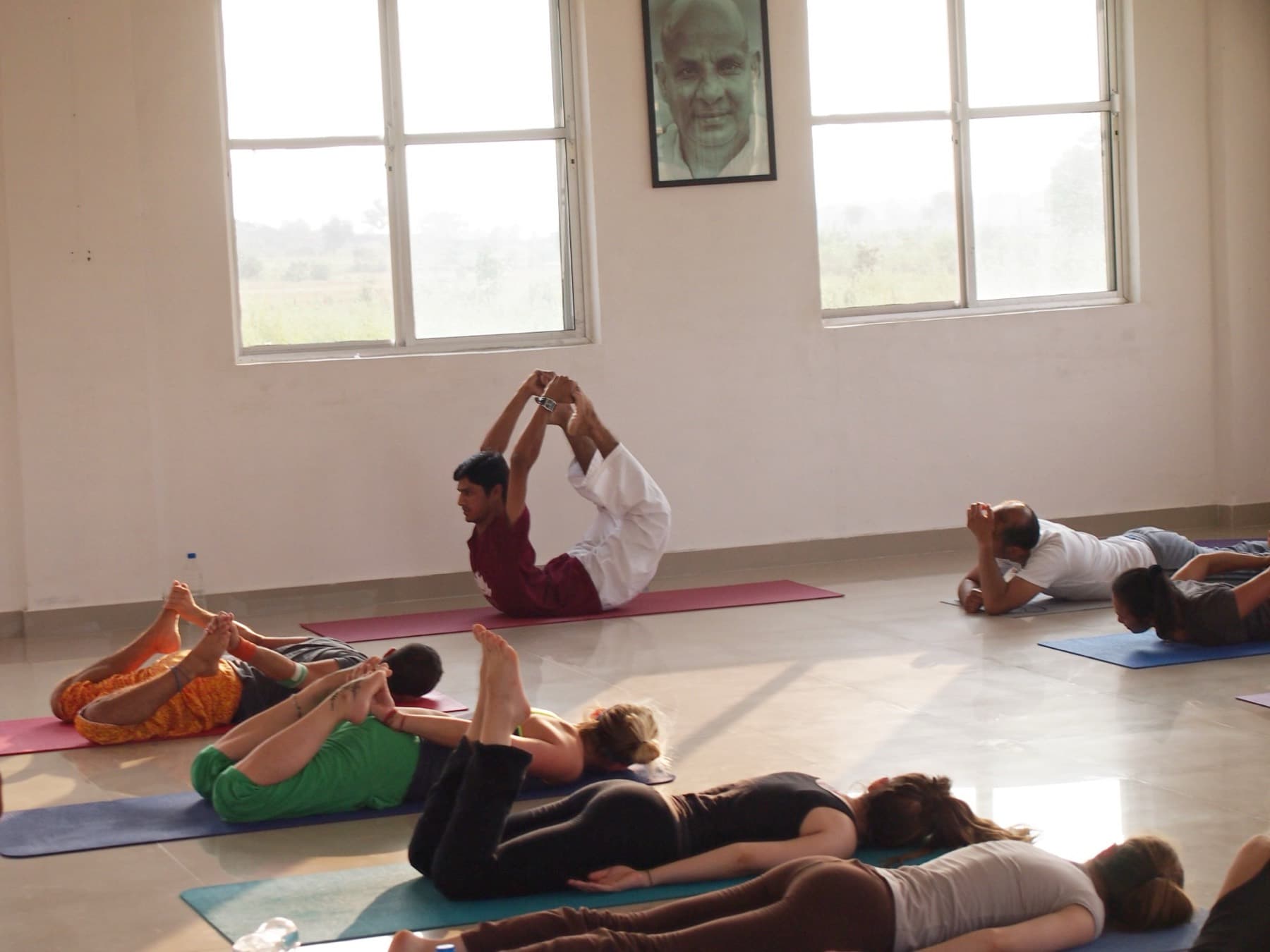 Yogi Madhav demonstrating bow pose to students in a white hall in India during a teacher training