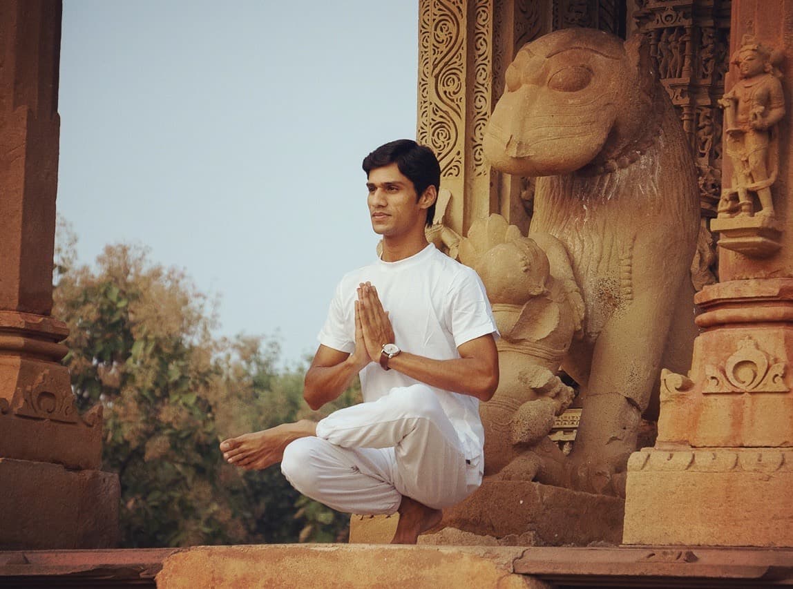 Yogi Madhav balancing in namaste beside a carved stone lion at a Khajuraho temple