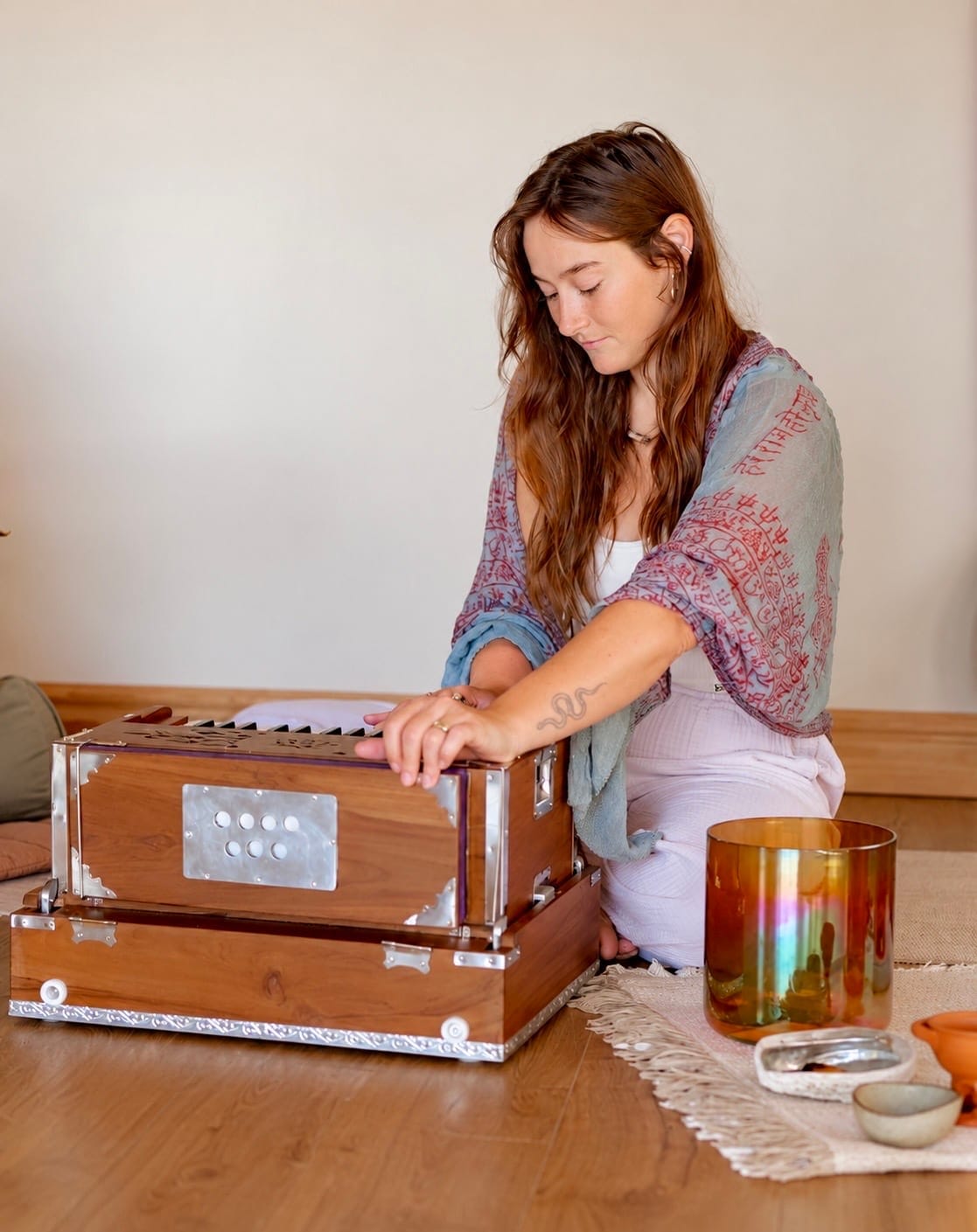 A woman seated on the floor playing a harmonium, with a singing bowl beside her