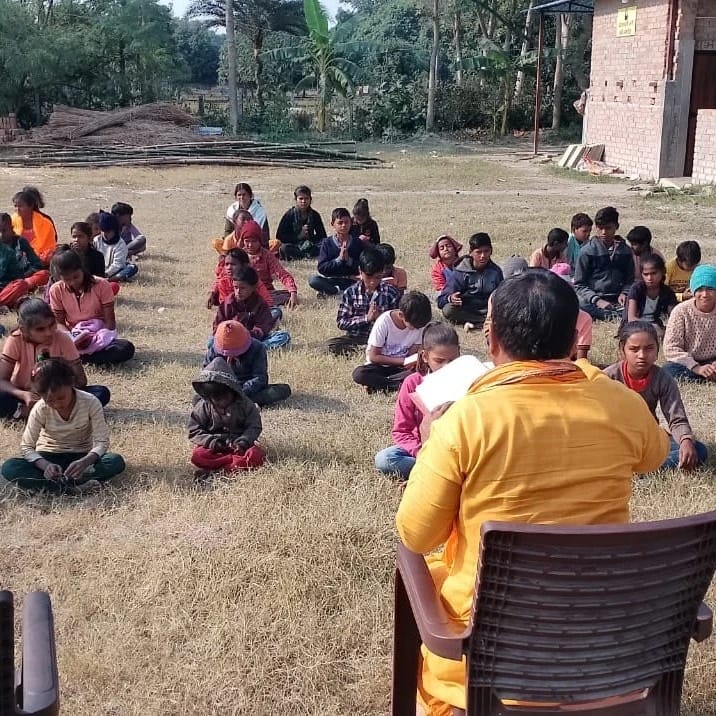 Children sitting on the ground for an outdoor class with their teacher