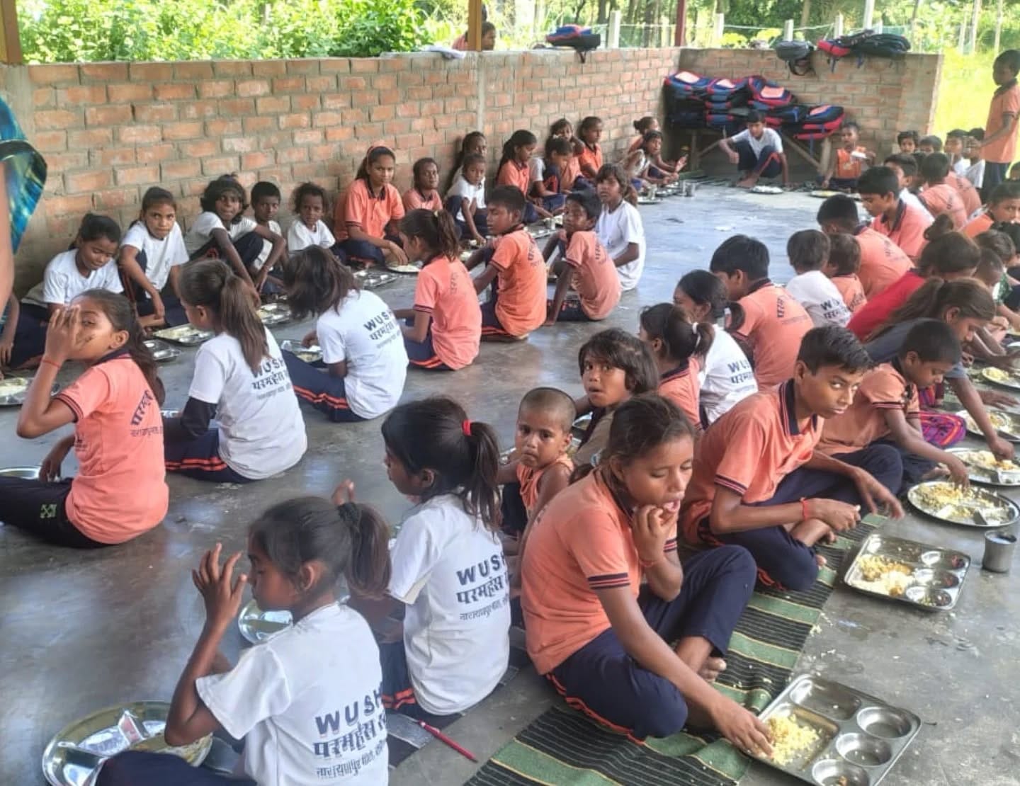 Children in school uniforms sitting in rows, sharing a meal together