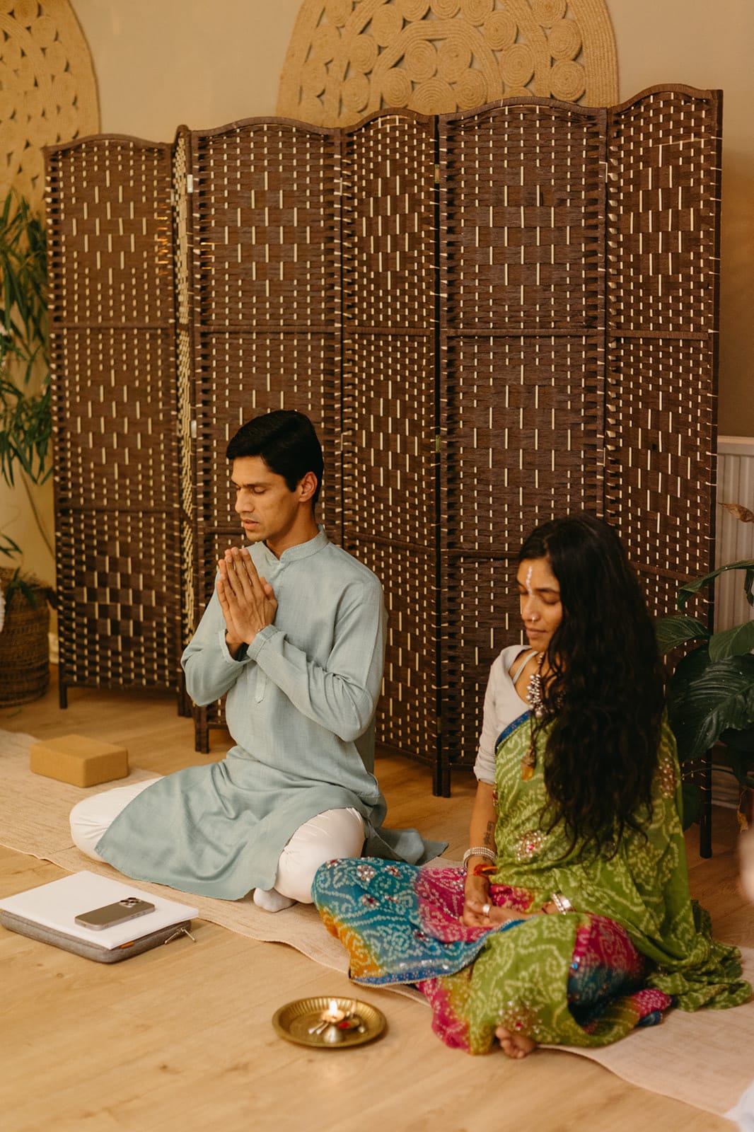 Yogi Madhav greets the circle with folded hands, seated beside a teacher in a green sari