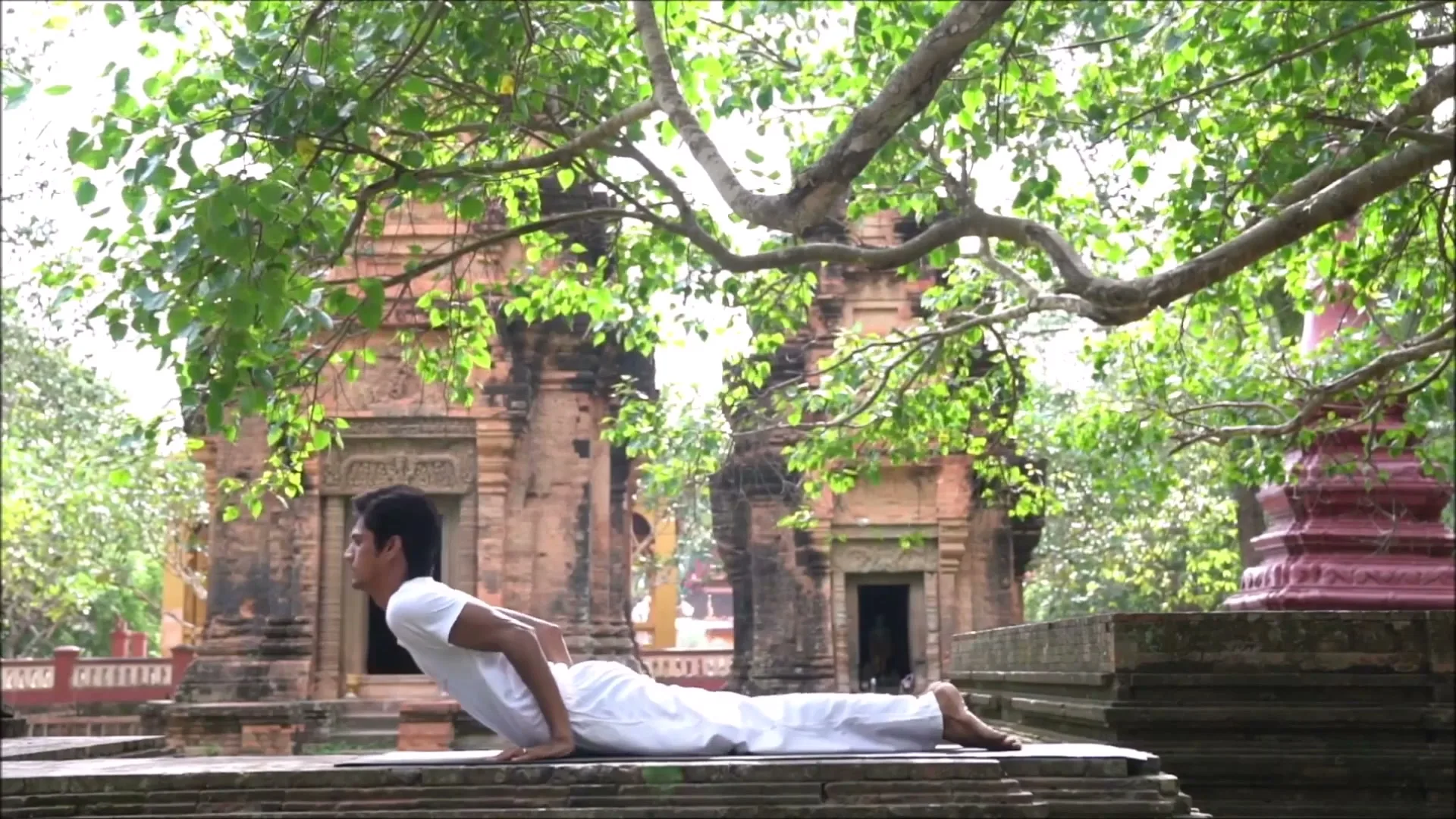 A yogi in white moves through Surya Namaskar, the sun salutation, beside an ancient temple.