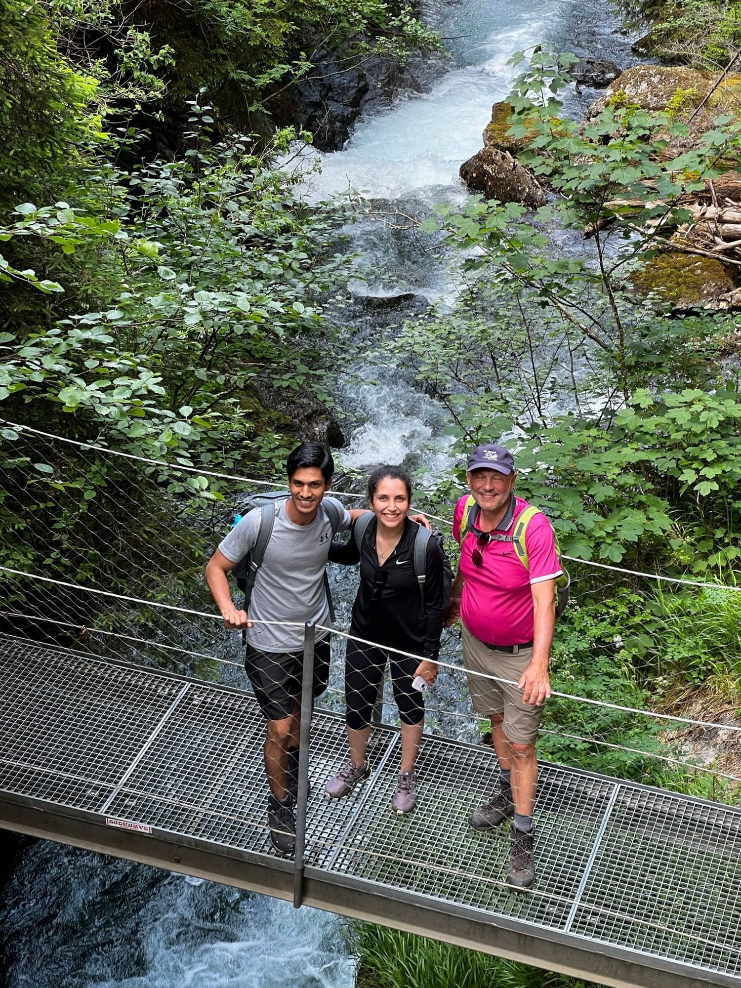 Three hikers on a suspension bridge in front of a waterfall