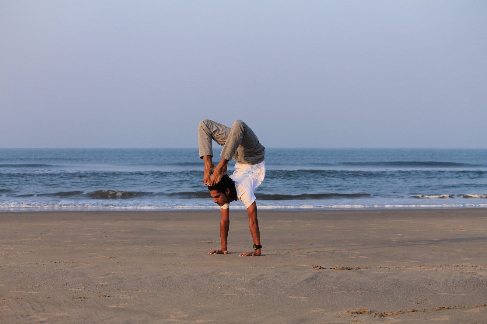 A yogi practising an arm balance on the beach