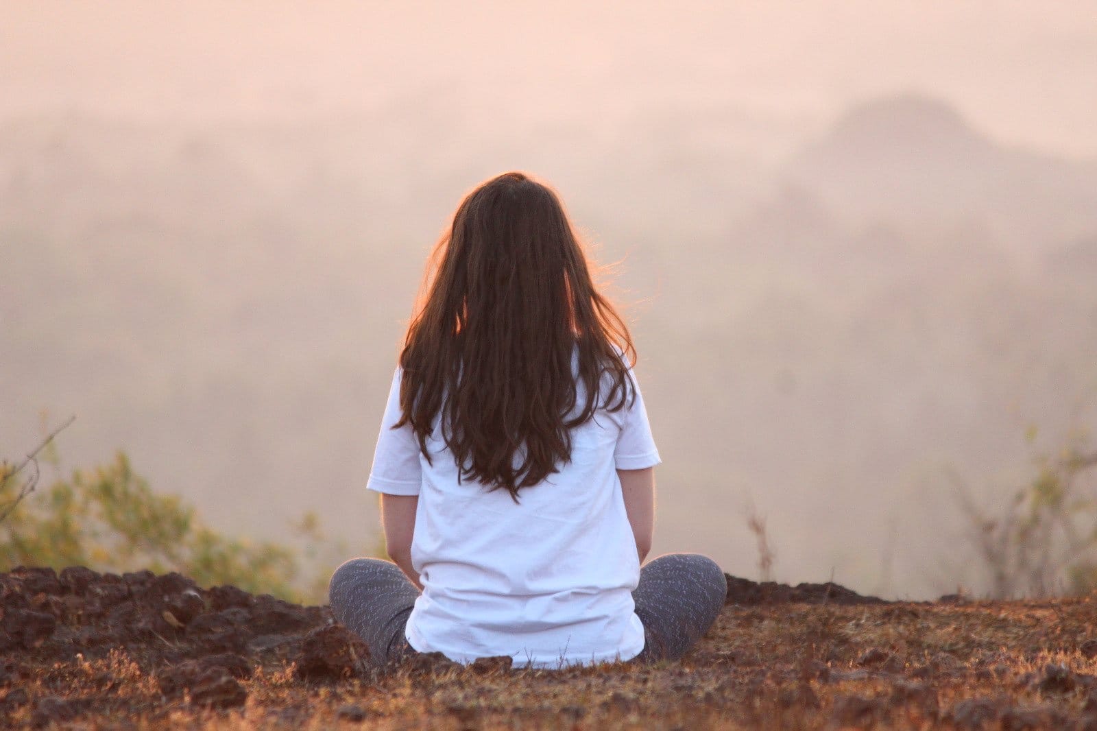 A woman meditating on a hilltop above morning mist
