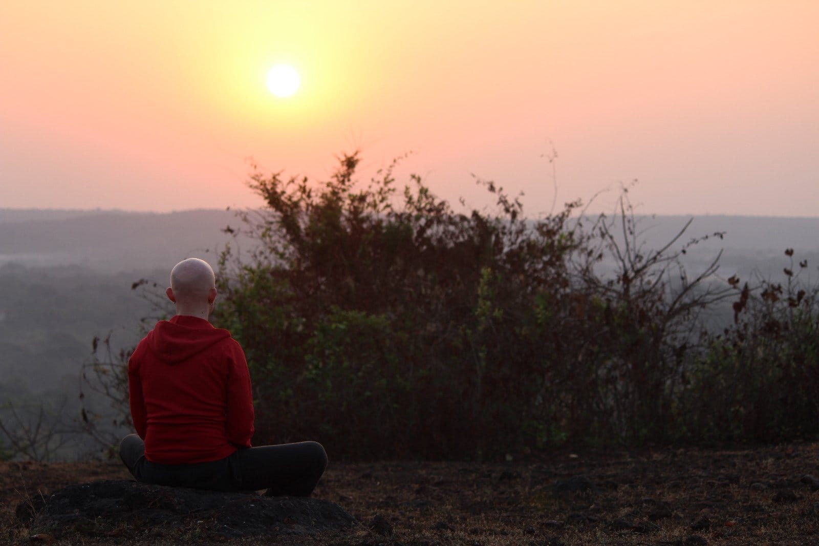 A man meditating on a hillside at sunset
