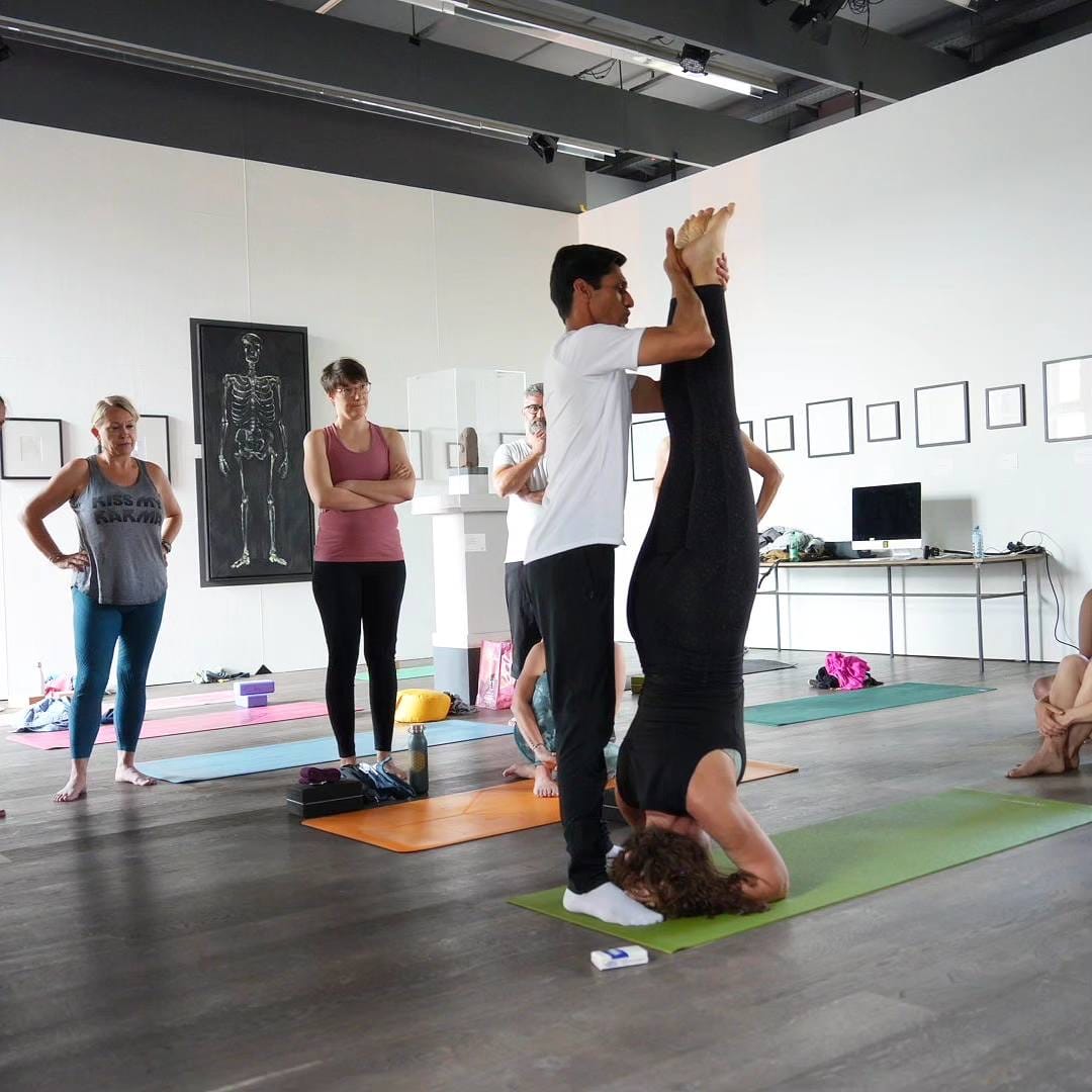 Yogi Madhav supporting a student in headstand at a workshop in Austria