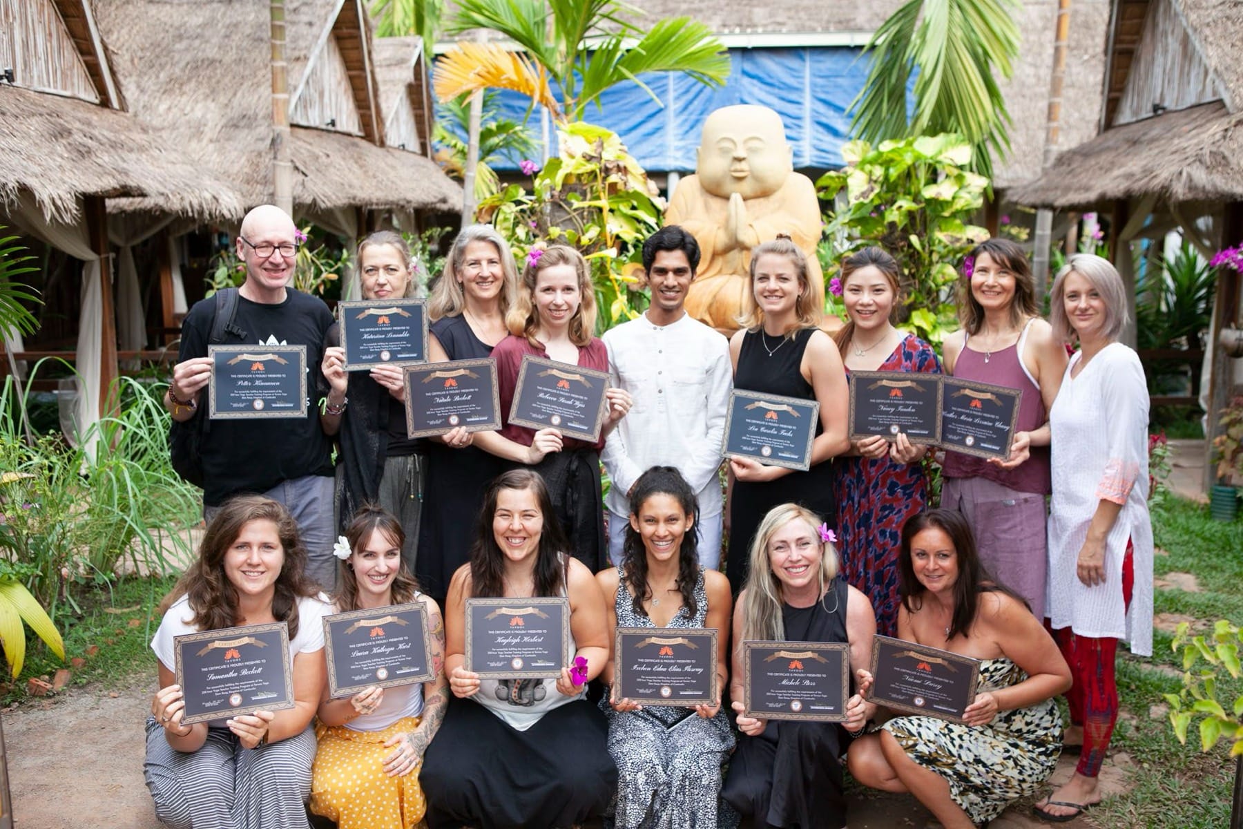 Graduates holding certificates in a garden with Yogi Madhav, in front of a stone statue in Cambodia