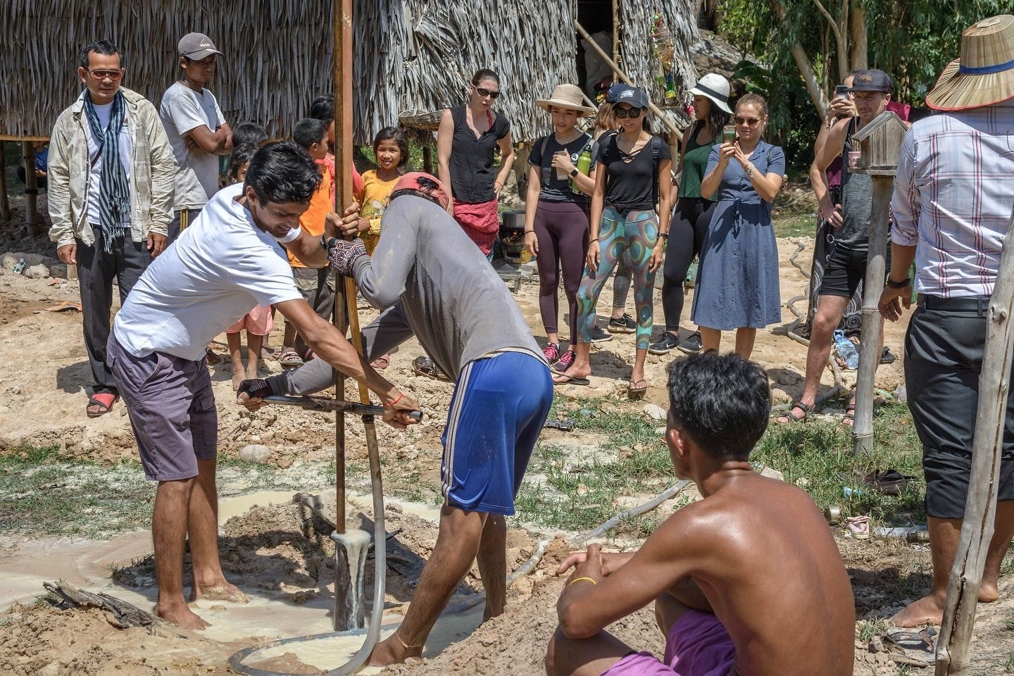 Yogi Madhav helping to drill a well while students and villagers watch, in Cambodia