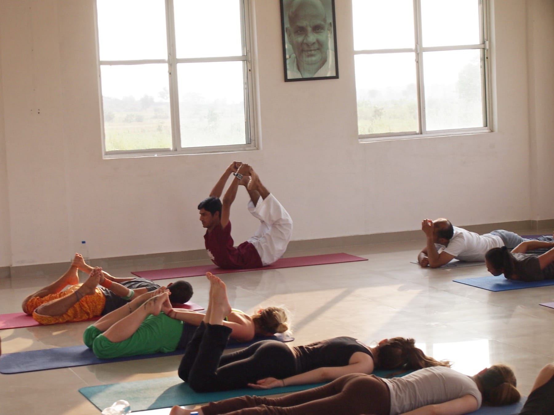 Yogi Madhav demonstrating bow pose to students in a white hall in India during a teacher training