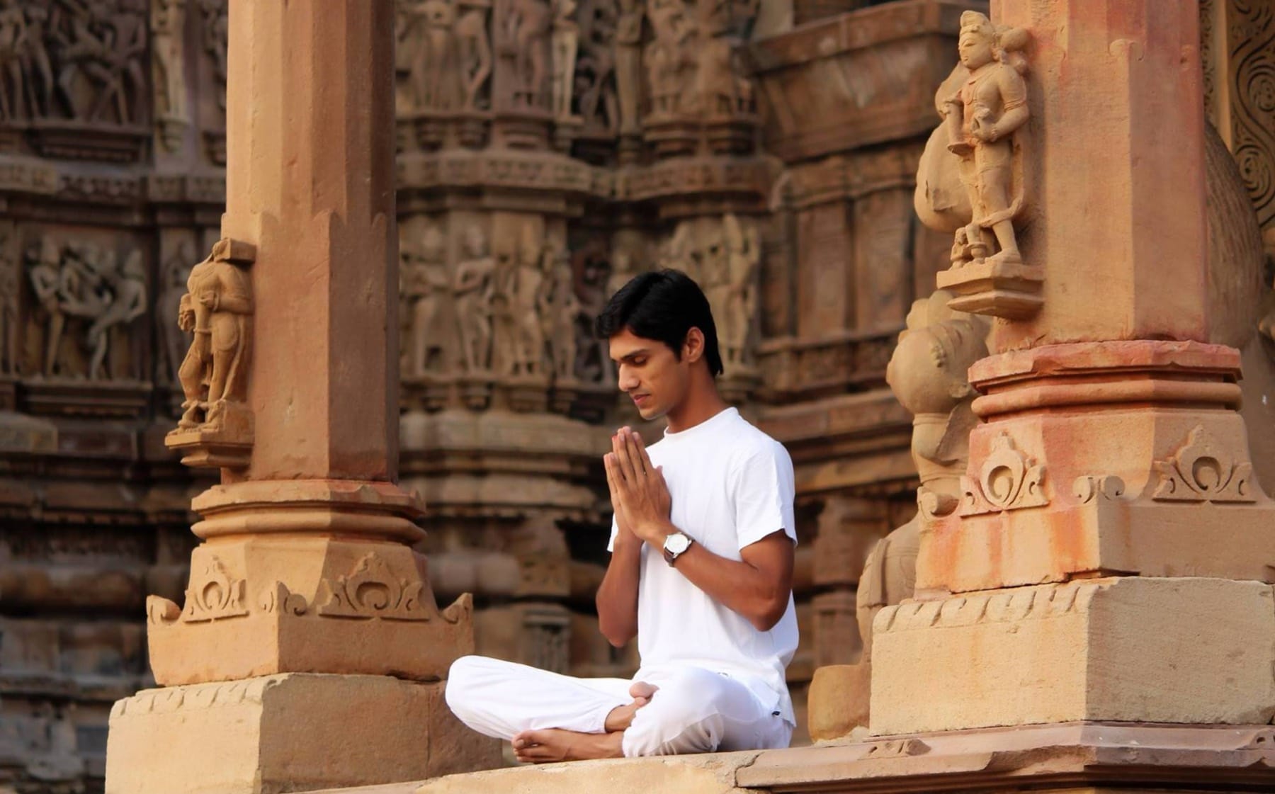 Yogi Madhav seated in prayer between carved sandstone pillars at Khajuraho
