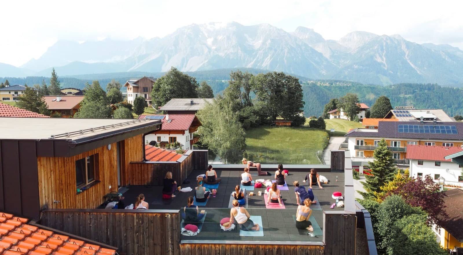 Group yoga practice on a rooftop terrace facing the Dachstein mountains