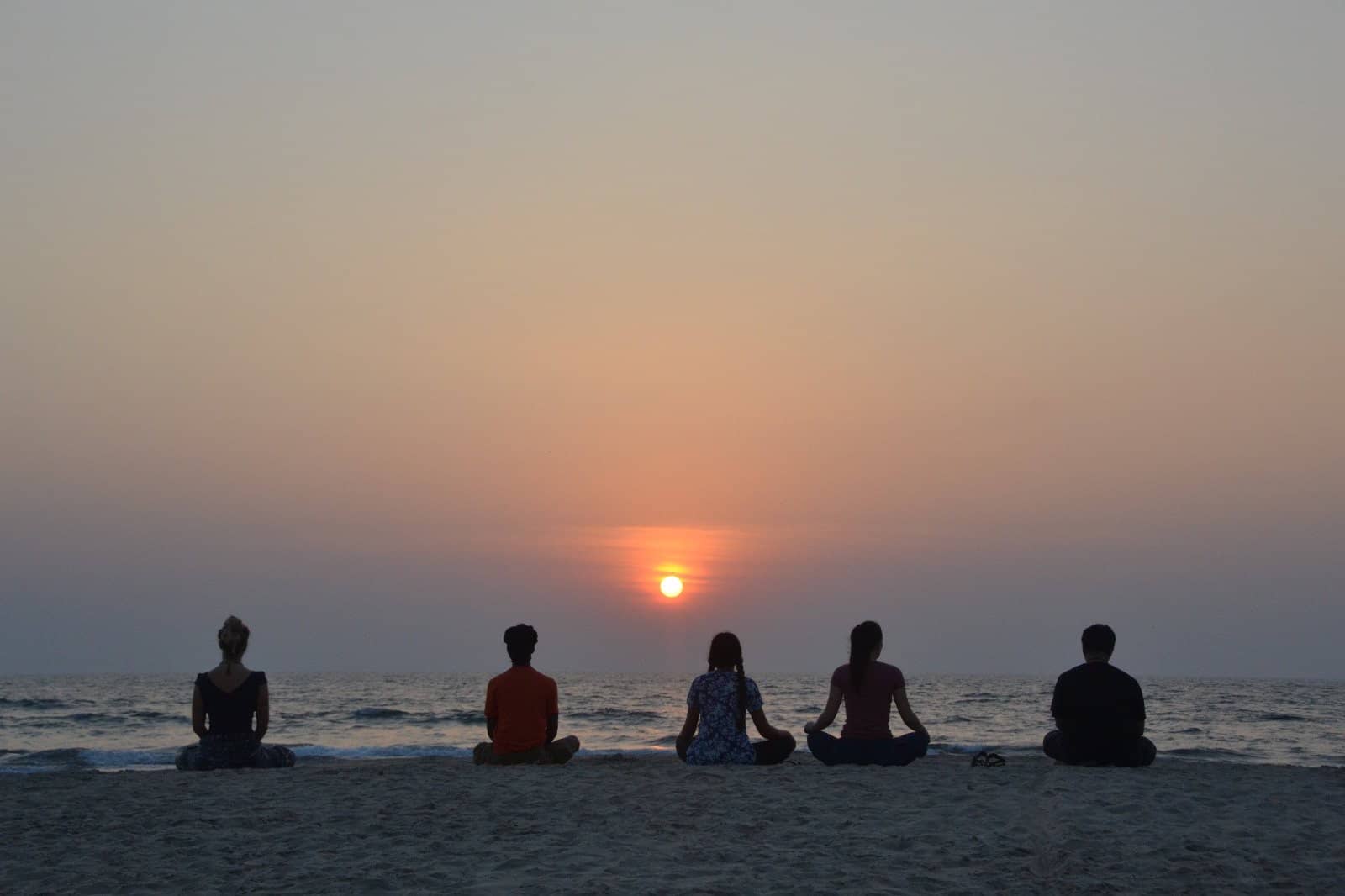 Five people meditating on a beach in Goa as the sun sets over the sea