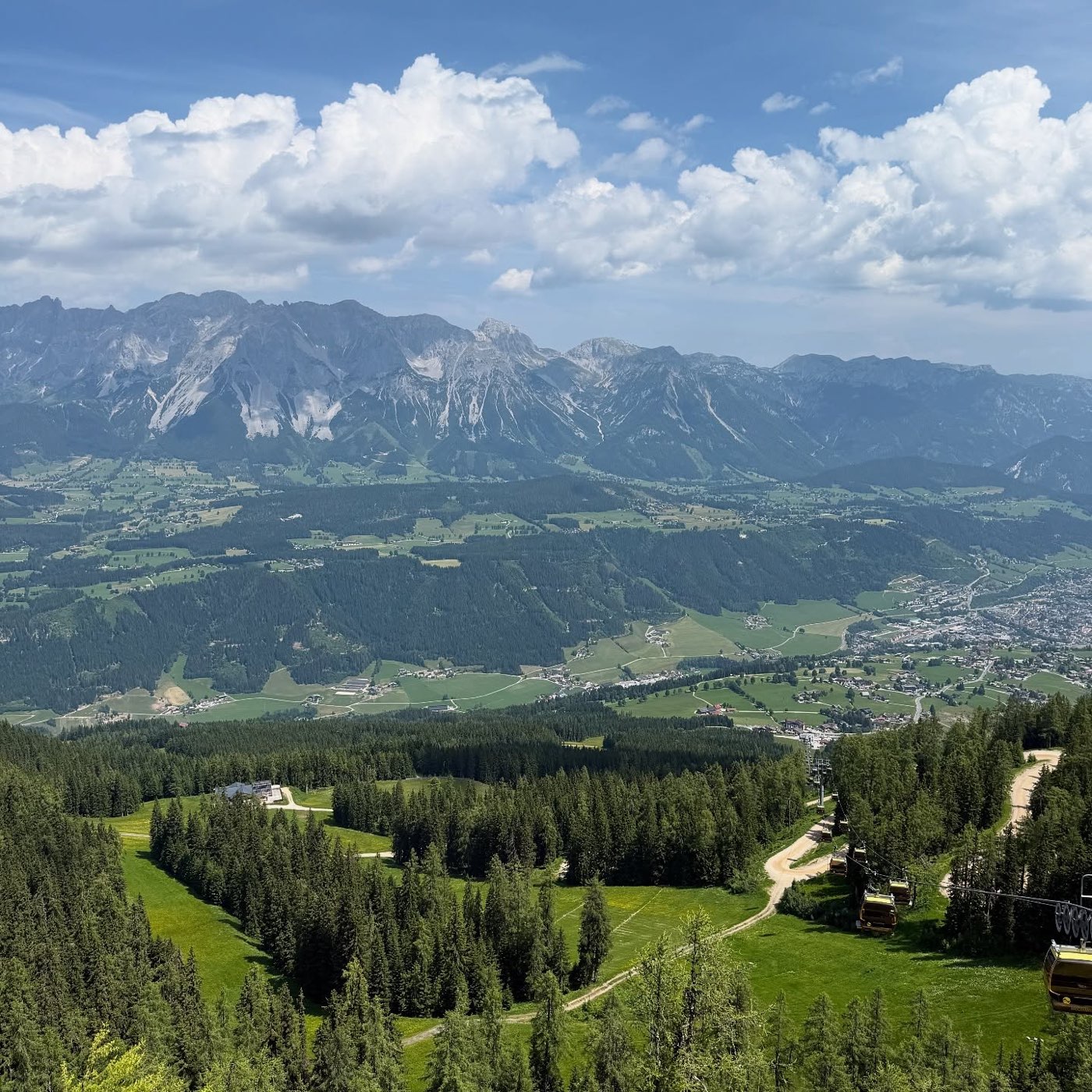The Dachstein range above a green valley of forest and meadows near Schladming, with cable cars in the foreground